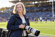 Fiona Goodall holding a professional camera at a rugby stadium in New Zealand