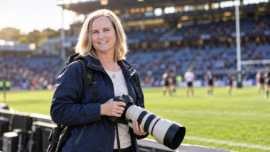 Fiona Goodall holding a professional camera at a rugby stadium in New Zealand